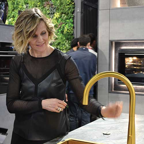 Linda Barker looking at a gold sink and tap combination on Caple's stand at kbb Birmingham